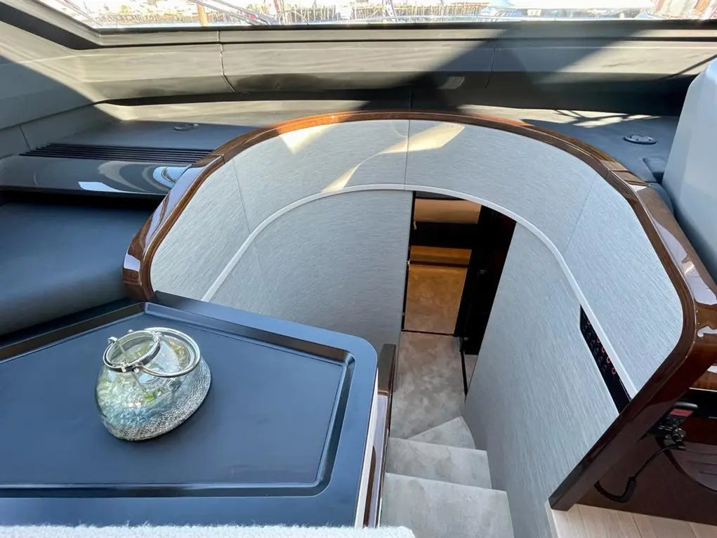 Luxury yacht interior featuring a curved stairway, decorative glass vase on a table, and natural light streaming in.